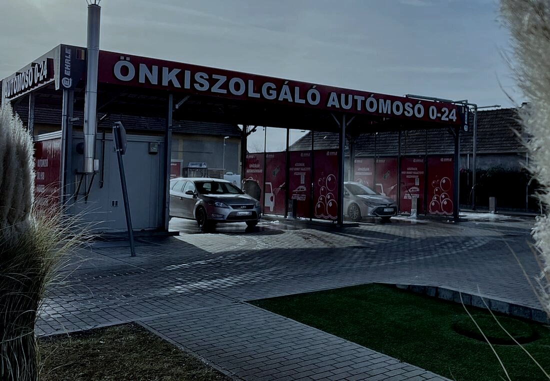 Ugyanaz a kapu alkonyatkor, alacsonyan járó nappal, az ÖNKISZOLGÁLÓ AUTÓMOSÓ 0–24 felirattal.